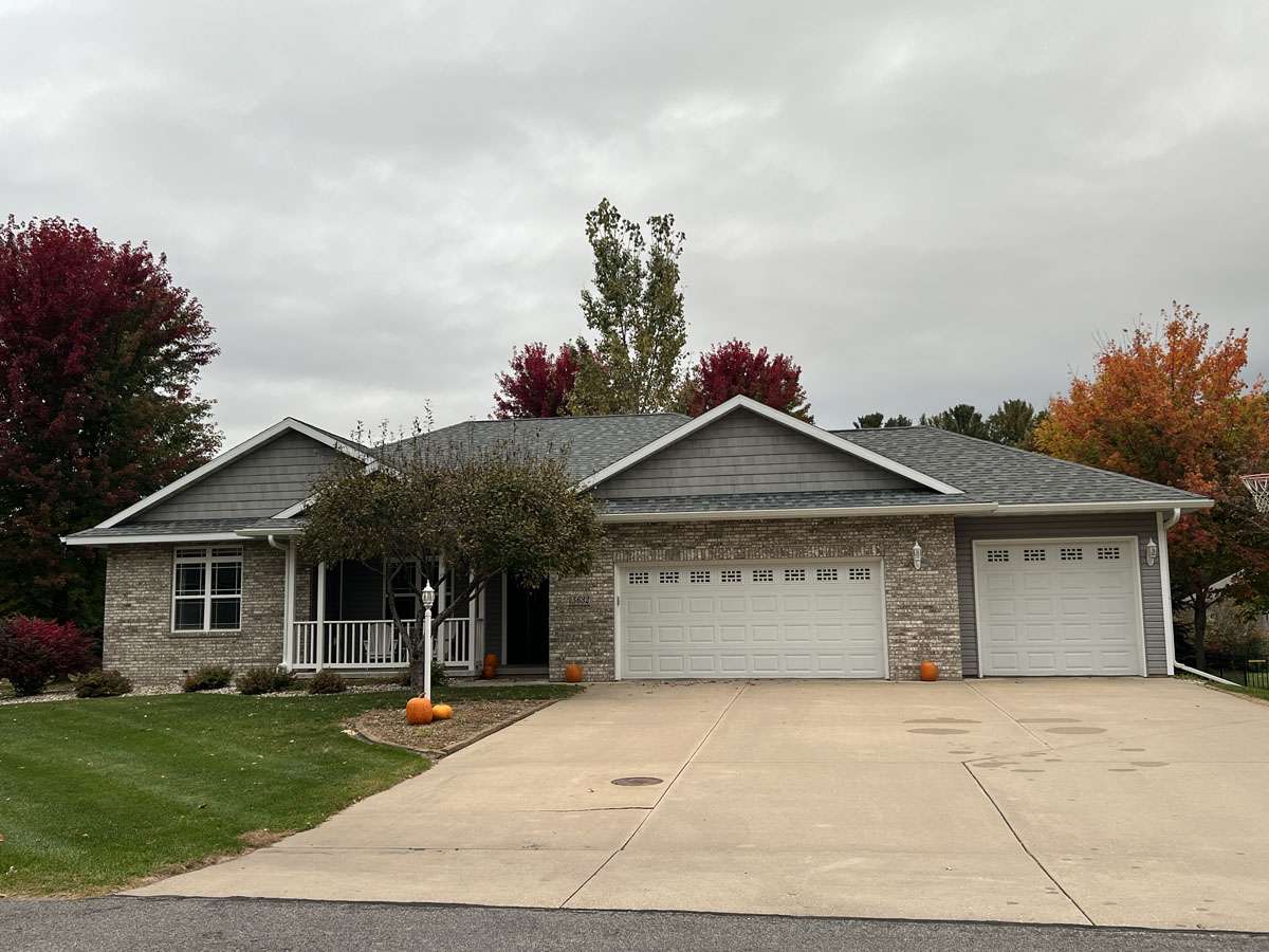 Front view of house with tall fall trees behind it.